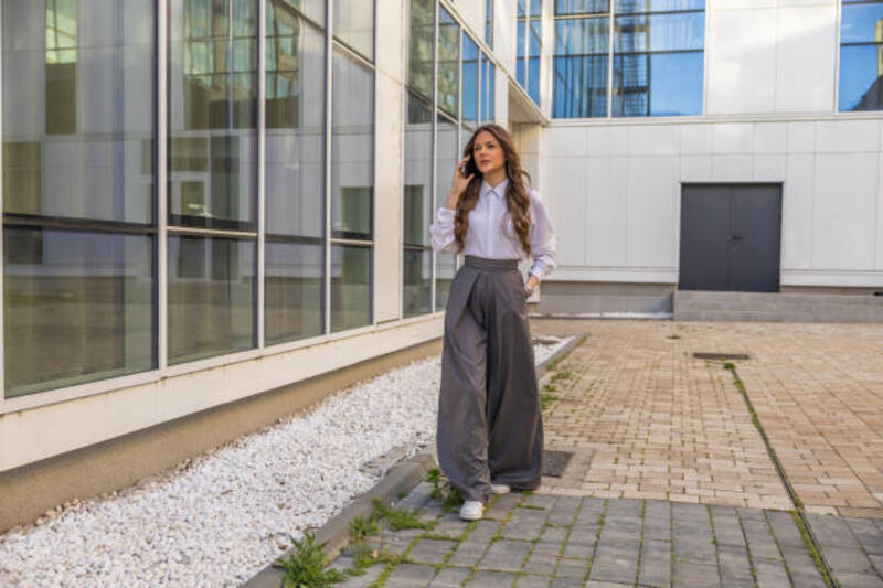 wanita profesional muda dengan pakaian formal menggunakan ponsel dan pergi bekerja dalam perjalanan ke pertemuan, berjalan di jalan kota di antara gedung-gedung perkantoran. - kemeja besar dan kulot potret stok, foto, &amp; gambar bebas royalti