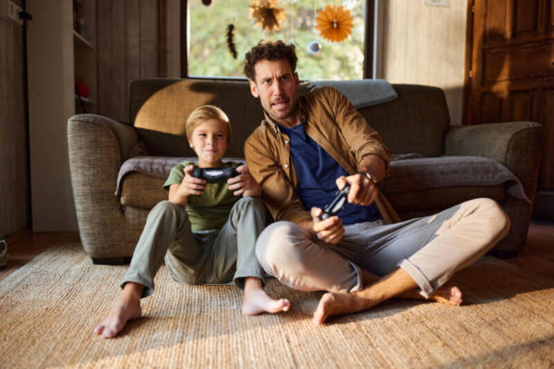 Playing video games at home! Carefree single father and his son having fun while playing video games on TV in the living room. game controller stock pictures, royalty-free photos &amp; images
