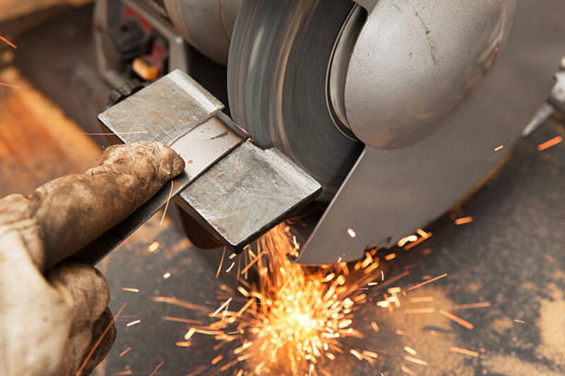 Bench Grinder, Grinding Metal with Sparks A bench grinder is being used to grind a steel bar. The grinding wheel is spinning with sparks flying downward. The bar is held with a gloved hand and extended finger. bench grinder stock pictures, royalty-free photos &amp; images
