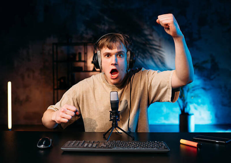 gamer yang bersemangat merayakan kemenangan sambil streaming dengan headphone dan mikrofon dalam pengaturan game yang gelap dan murung. - gamers use condenser potret stok, foto, & gambar bebas royalti