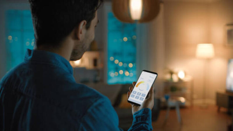 Young Handsome Man is Setting up Comfortable Bedroom Conditions with Voice Command to Smart Home Application on His Smartphone. It