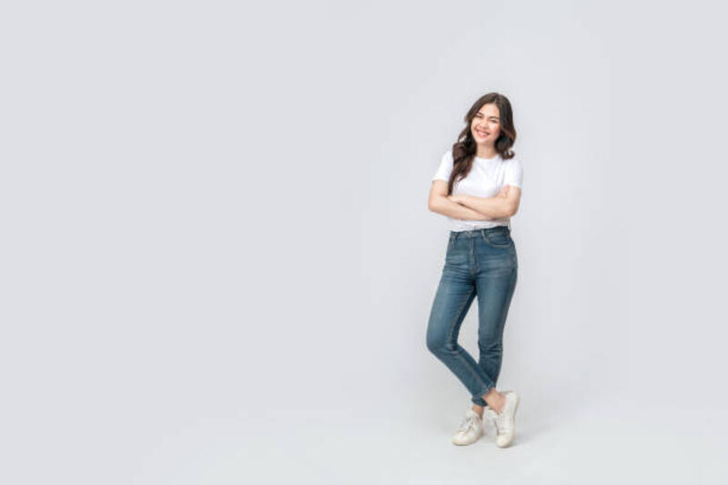 panjang penuh wanita asia yang percaya diri tersenyum dengan pakaian kasual dengan t-shirt putih dan jeans, berdiri dengan lengan dan kaki disilangkan dengan latar belakang putih yang terisolasi. - white shirt and jeans potret stok, foto, &amp; gambar bebas royalti