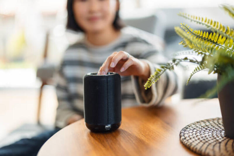 Enjoying Smart Technology at Home A mid adult Asian woman interacts with a portable smart speaker on a wooden table amidst the comfort of her modern living room. speaker portable stock pictures, royalty-free photos & images