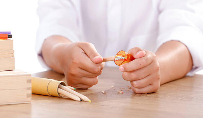 Young student hands hands sharpening pencils with a sharpener. Young student hands hands sharpening pencils with a sharpener. Close up of child hands in white T-shirt on wooden desk. Copy space. pencil sharpener stock pictures, royalty-free photos &amp; images