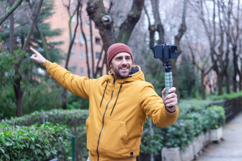 Influencer creating content with smartphone gimbal in the city park Young man vlogging and pointing while holding a smartphone on a gimbal in a city park tripod stock pictures, royalty-free photos &amp; images