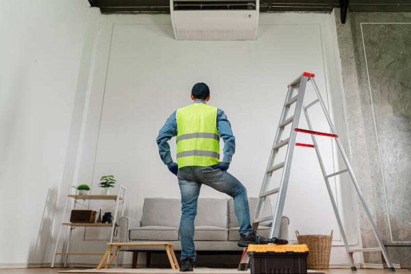 teknisi profesional mengenakan rompi pengaman berdiri di tangga di dalam ruangan modern, siap memasang unit ac untuk peningkatan kenyamanan rumah - fixture wall potret stok, foto, &amp; gambar bebas royalti