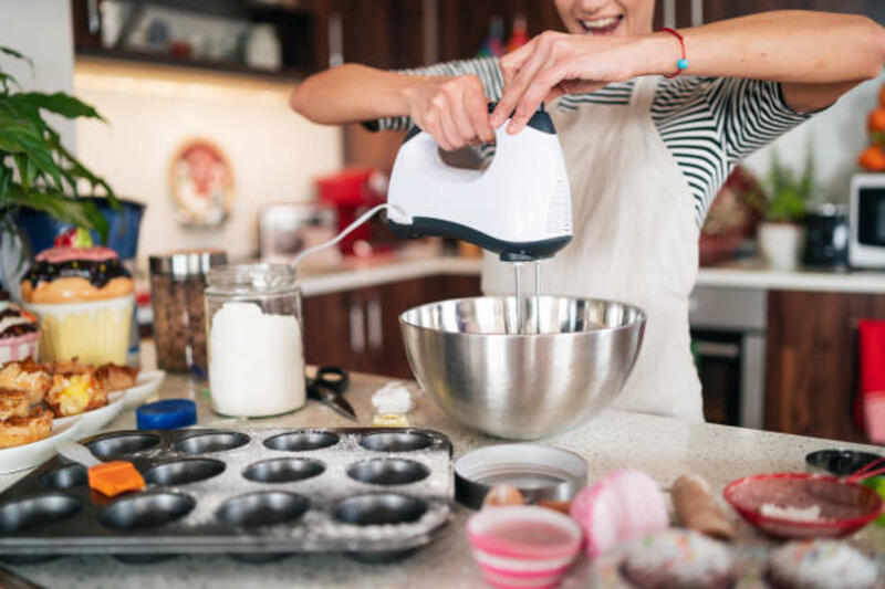 Tangan wanita memegang mixer, whipping cream dalam mangkuk logam untuk membuat dekorasi pada cupcakes buatan sendiri di dapurnya.