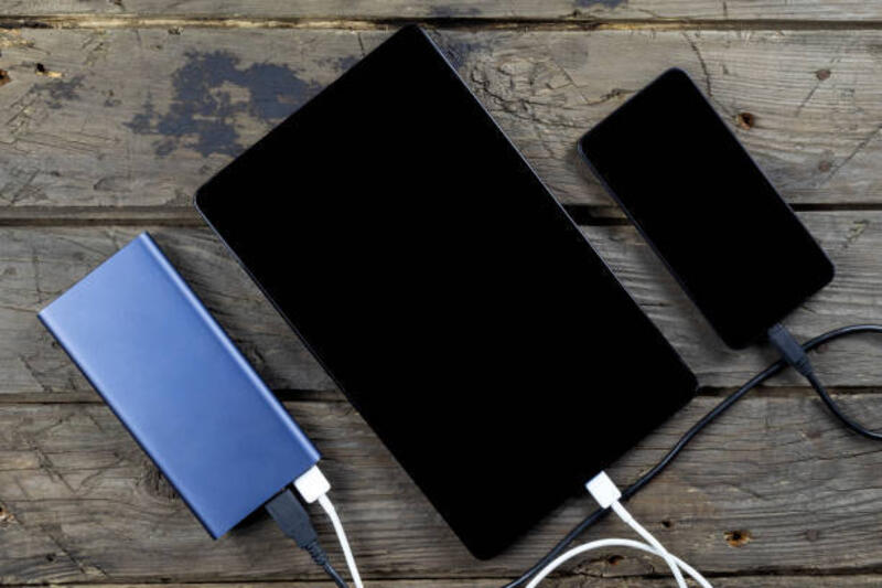 Perangkat seluler smartphone, tablet, dan power bank di atas meja kayu