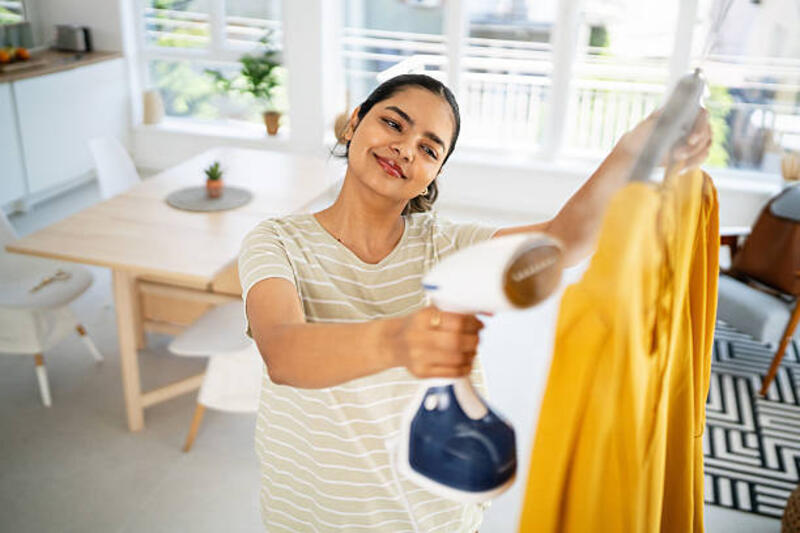 wanita muda dengan hati-hati menyetrika pakaian dengan setrika uap dalam kenyamanan rumahnya - iron steamer potret stok, foto, &amp; gambar bebas royalti