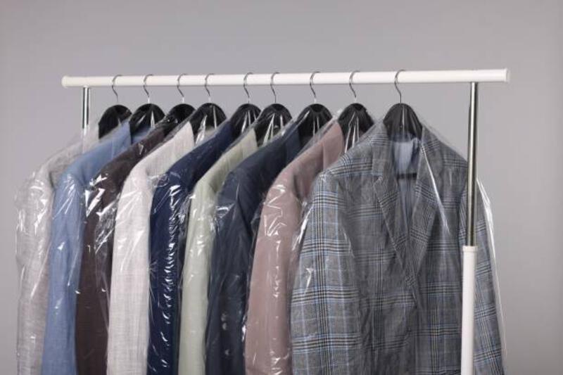 layanan dry-cleaning. banyak pakaian berbeda dalam kantong plastik tergantung di rak dengan latar belakang abu-abu - mencuci kemeja potret stok, foto, &amp; gambar bebas royalti