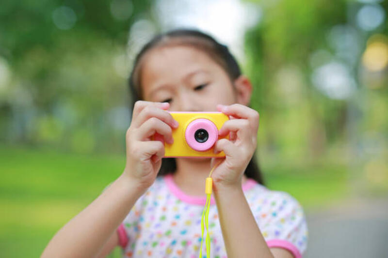 Gadis kecil close-up dengan mainan kamera digital di taman luar ruangan. Fokus pada kamera di tangan.