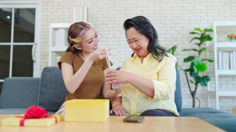 putri muda asia terkejut memberikan hadiah ulang tahun kepada ibu sambil duduk di sofa di rumah. wanita muda memberikan hadiah ulang tahun kepada ibu. konsep keluarga bahagia, konsep hari ibu - memberikan mama perhiasan potret stok, foto, &amp; gambar bebas royalti