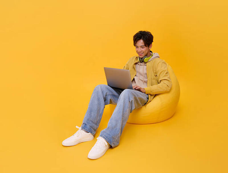 Happy handsome Asian businessman using laptop While his sitting relax on beanbag isolated on yellow background. Happy handsome Asian businessman using laptop While his sitting relax on beanbag isolated on yellow background. bean bag stock pictures, royalty-free photos &amp; images