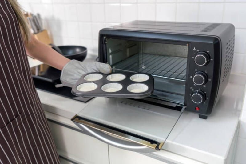 seseorang dengan celemek dan sarung tangan oven, menempatkan nampan muffin dengan adonan ke dalam oven pemanggang roti hitam di dapur putih. - oven listrik potret stok, foto, &amp; gambar bebas royalti