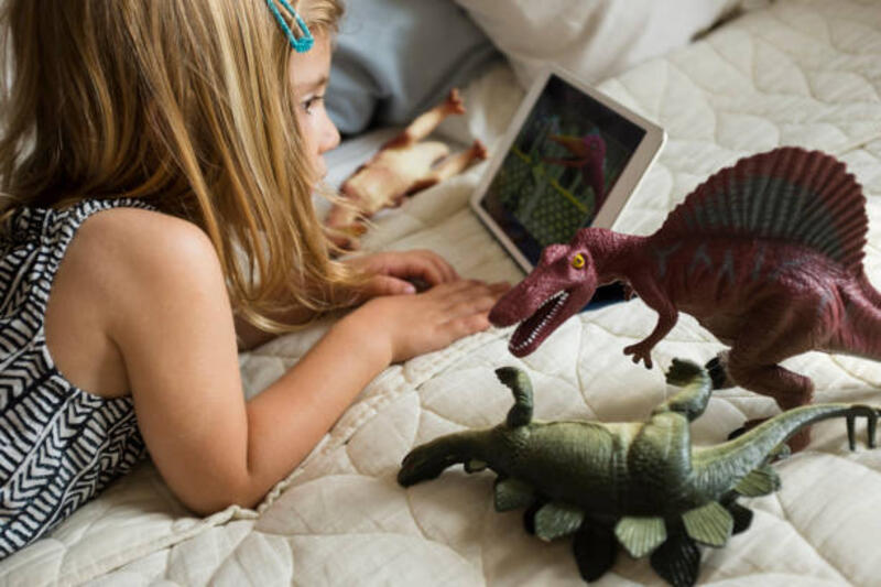 caucasian-girl-laying-on-bed-with-toy-dinosaurs-using-digital-tablet.jpg (612×408)