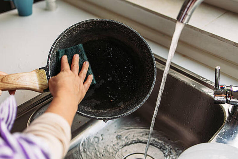 Close-up tangan wanita mencuci panci masak di bawah air mengalir