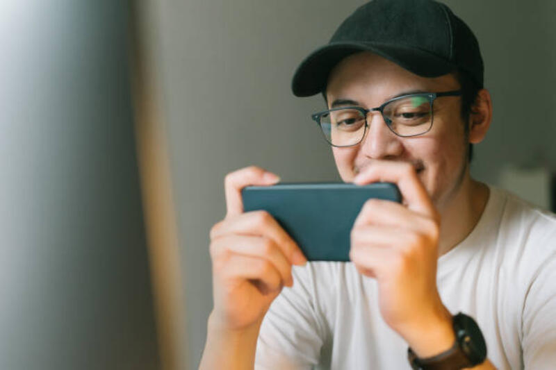 asian young man excited playing mobile game on his smartphone asian young man playing mobile game on his smartphone handheld game stock pictures, royalty-free photos &amp; images
