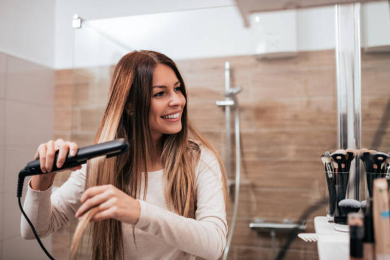 Beautiful young smiling woman using a hair straightener while looking into the mirror in bathroom. Beautiful young smiling woman using a hair straightener while looking into the mirror in bathroom. hair straightener stock pictures, royalty-free photos &amp; images