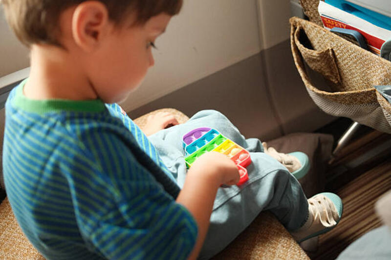 Child playing with fidget toy during airplane travel Young boy sitting in an airplane seat, keeping busy and entertained with a colorful Pop It fidget toy pop it toy stock pictures, royalty-free photos &amp; images