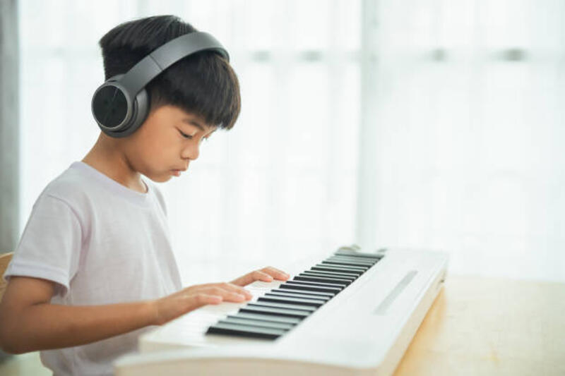 A young boy is playing the keyboard with headphones on. He is focused on the music and he is enjoying himself A young boy is playing the keyboard with headphones on. He is focused on the music and he is enjoying himself playing keyboard stock pictures, royalty-free photos &amp; images