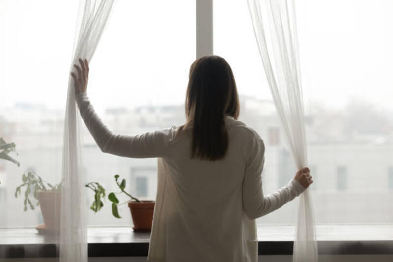 Rear view woman standing near window opening curtains looking outside Rear view woman stand near window in living room open curtains looking outside at rainy foggy weather. Welcoming start new day, apartment owner, rented flat concept, potted houseplants on windowsill gloomy day stock pictures, royalty-free photos &amp; images
