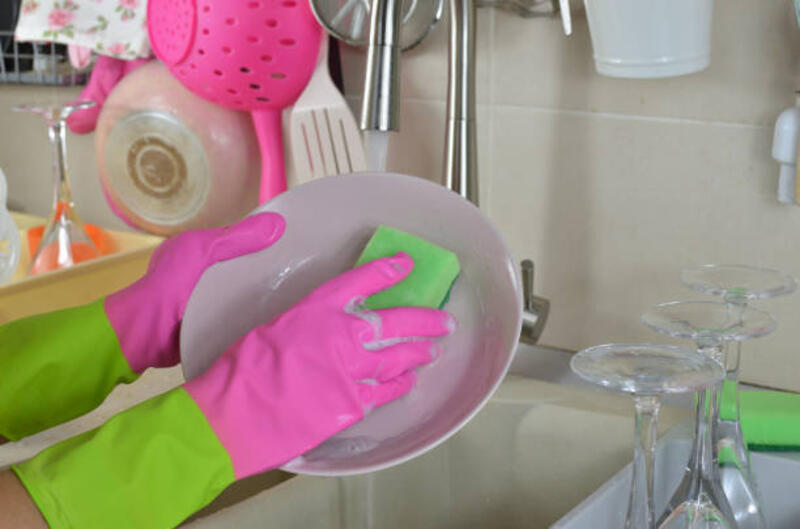 Tangan wanita dengan sarung tangan karet mencuci piring