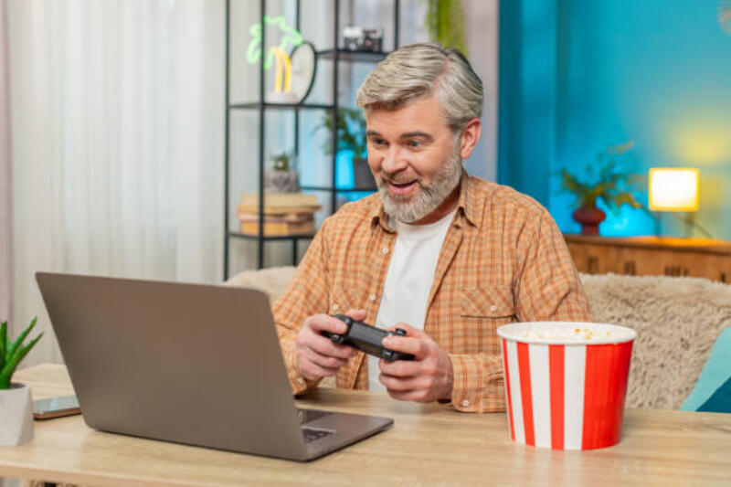 mature-man-sitting-at-table-with-laptop-and-gamepad-playing-video-games-and-eating-popcorn-at.jpg (612×408)