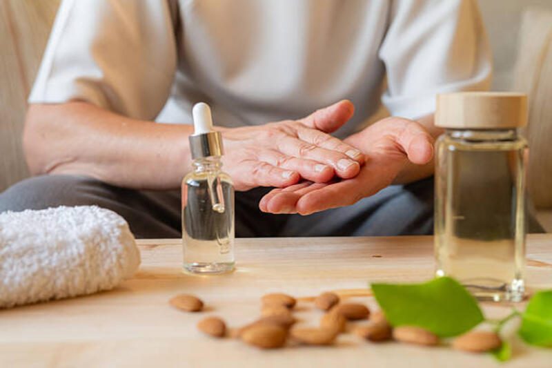 dewasa lansia mengoleskan minyak almond dengan lembut ke tangan, melembabkan dan menutrisi kulit kering untuk perawatan diri sehari-hari, hidrasi, dan relaksasi dalam momen spa rumah yang nyaman - almond oil potret stok, foto, &amp; gambar bebas royalti