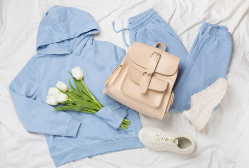 Flat lay dengan pakaian musim semi trendi dan bunga-bunga di latar belakang lembaran putih